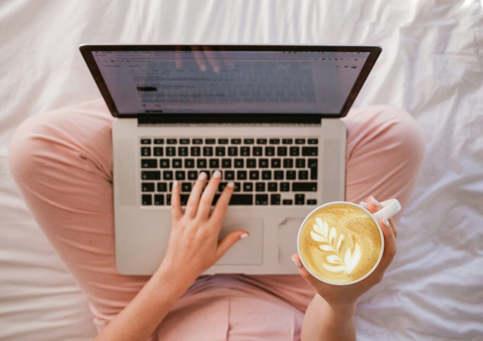 person using MacBook Pro and holding cappuccino