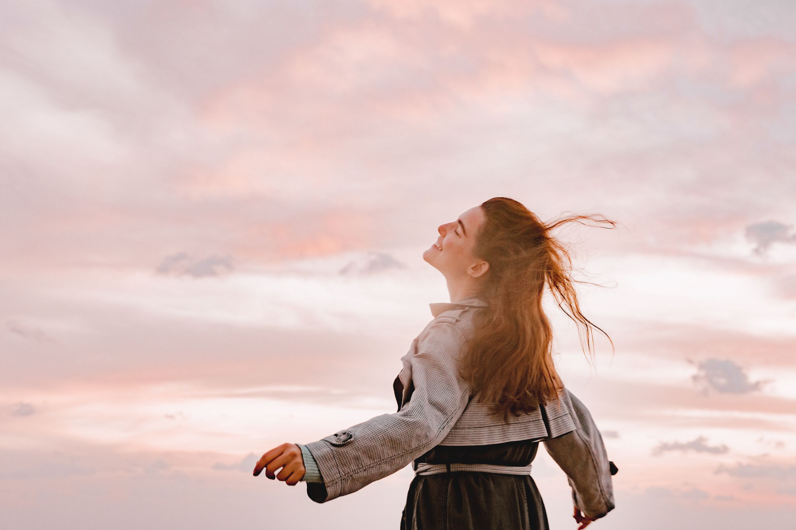 A woman joyfully embraces the sunset with arms spread in freedom, capturing serenity in nature.