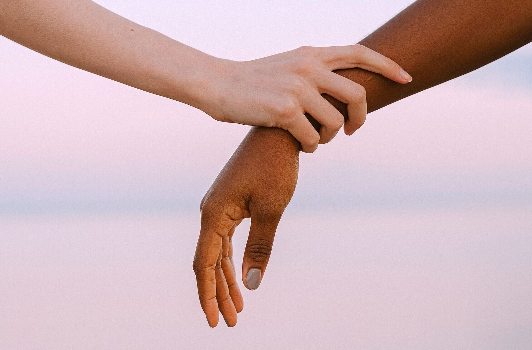 Close-up of two different skin toned hands holding gently against a serene sunset sky.