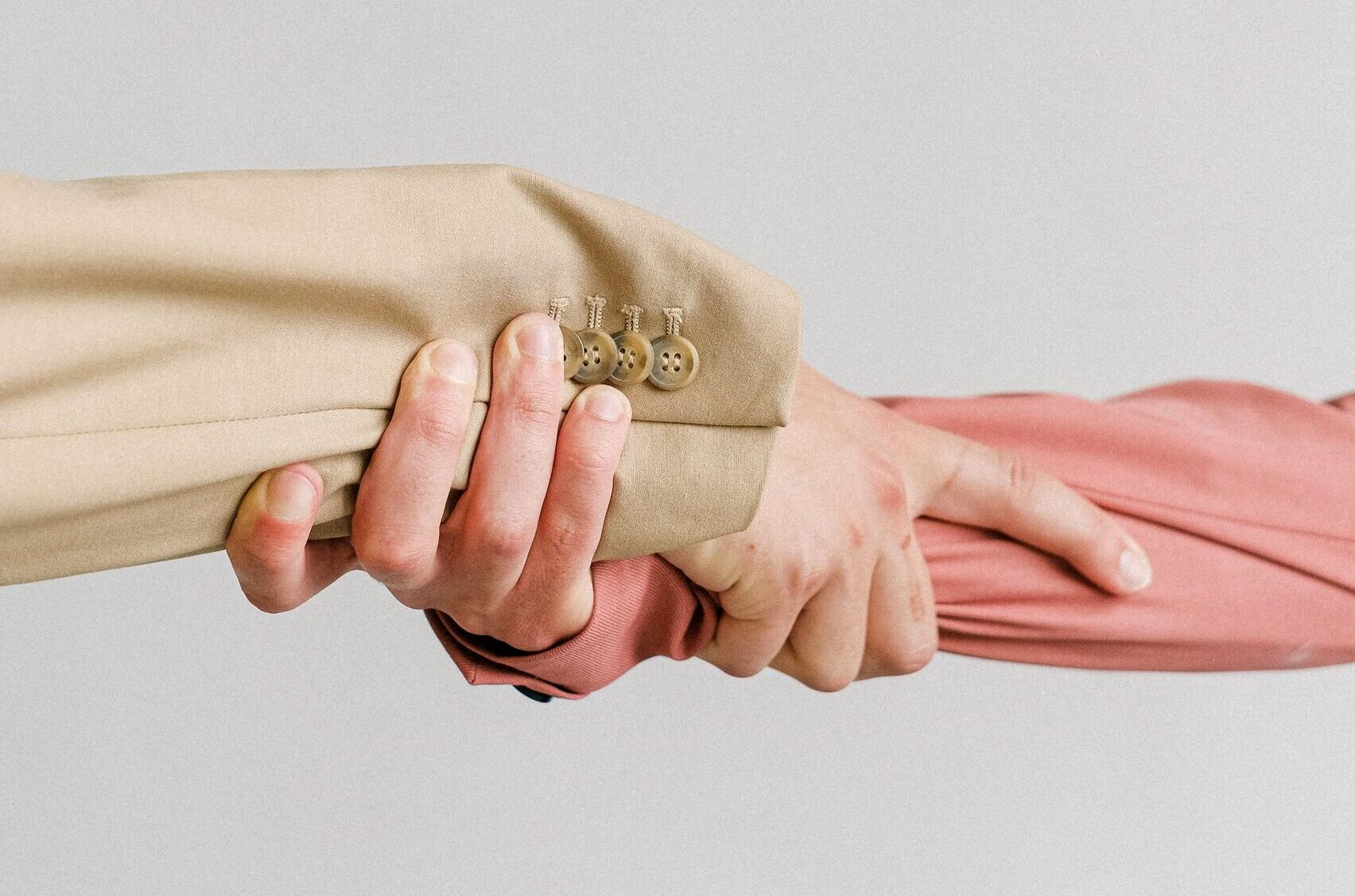 Two hands in formal attire grasping each other, symbolizing unity and support.
